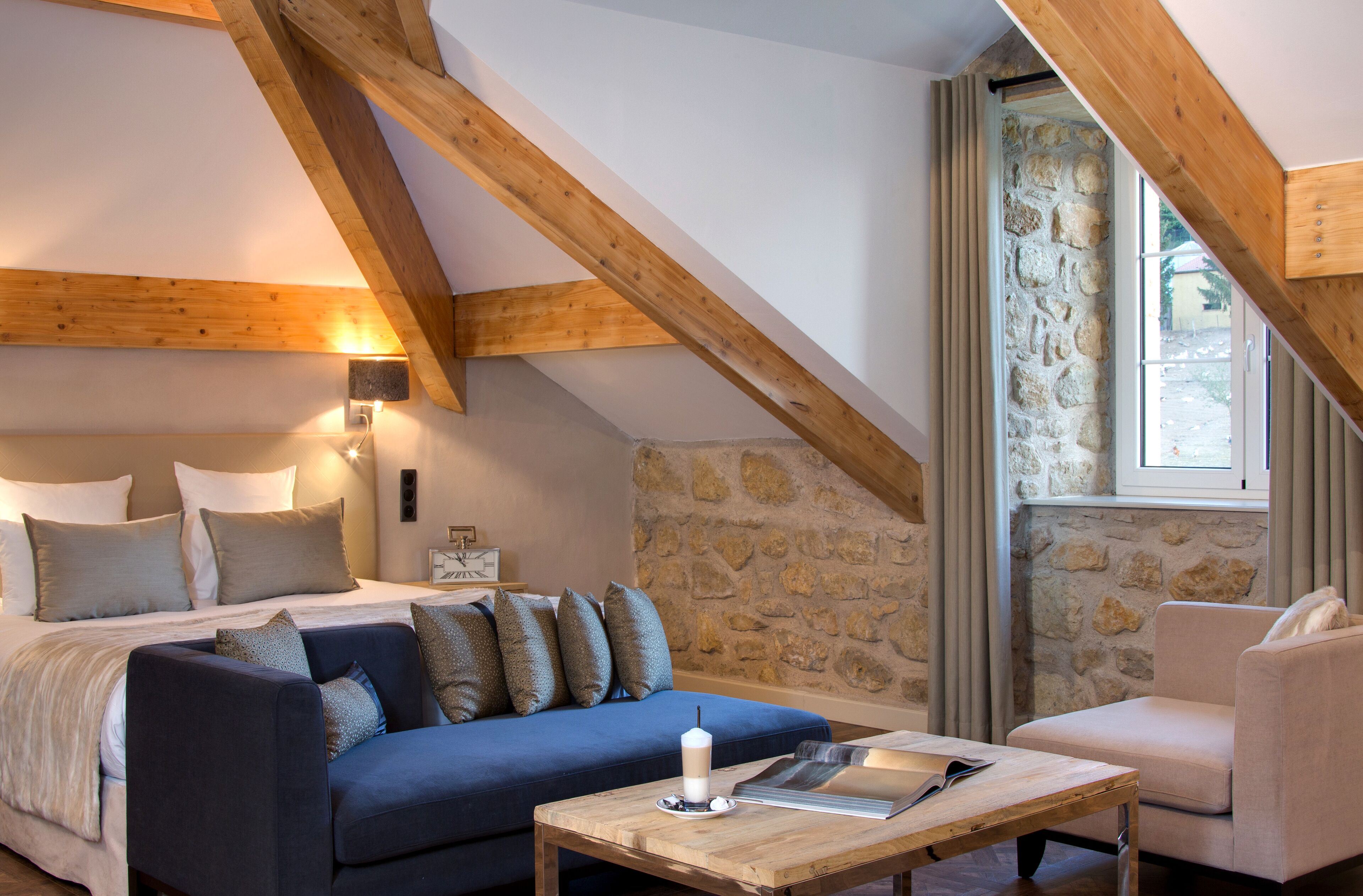 Una habitación acogedora con una cama, un sofá azul, una mesa de centro de madera y una pared de piedra.