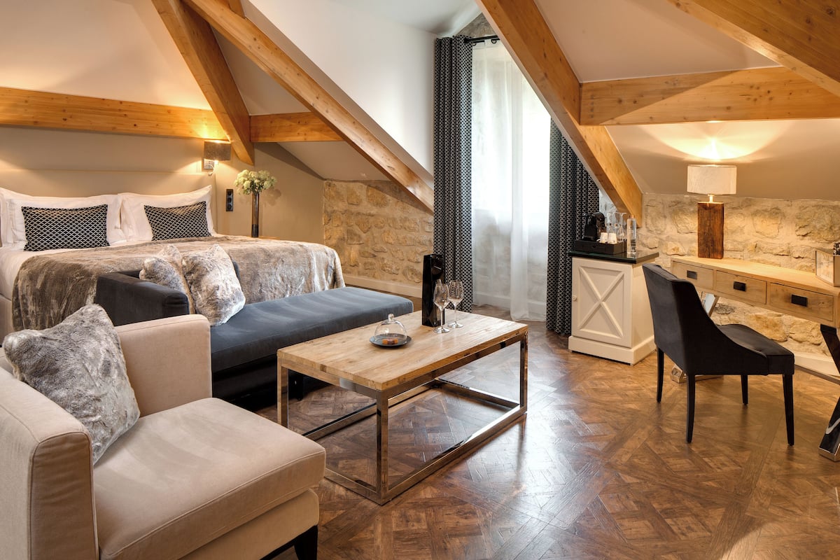 Een knus loft-slaapkamer met een groot bed, een bank, een salontafel en een eetgedeelte met een stenen muur en houten balken.