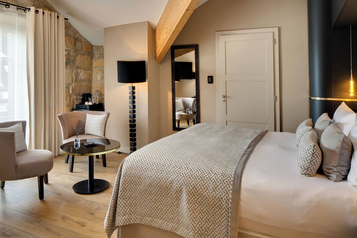 Een hotelkamer met een bed, een ronde tafel, een stoel, een lamp en een grote spiegel.