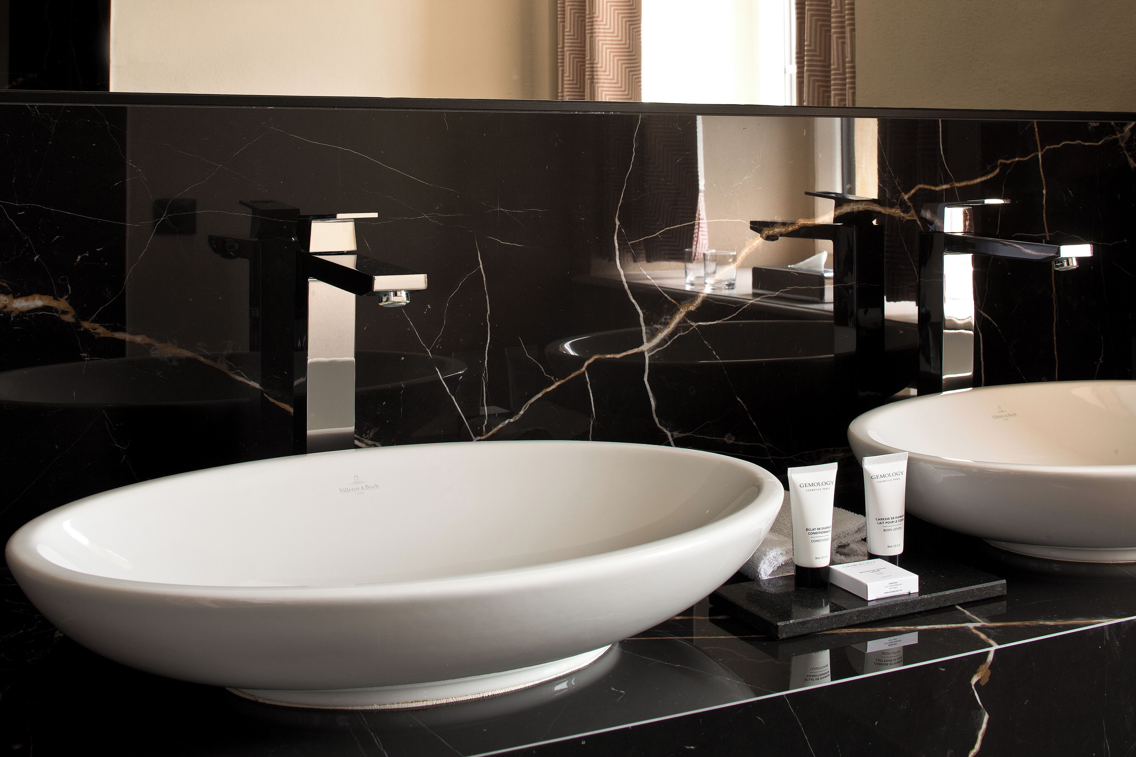 Une salle de bain moderne avec deux grands lavabos blancs, des comptoirs en marbre noir et un grand miroir qui reflète la pièce.