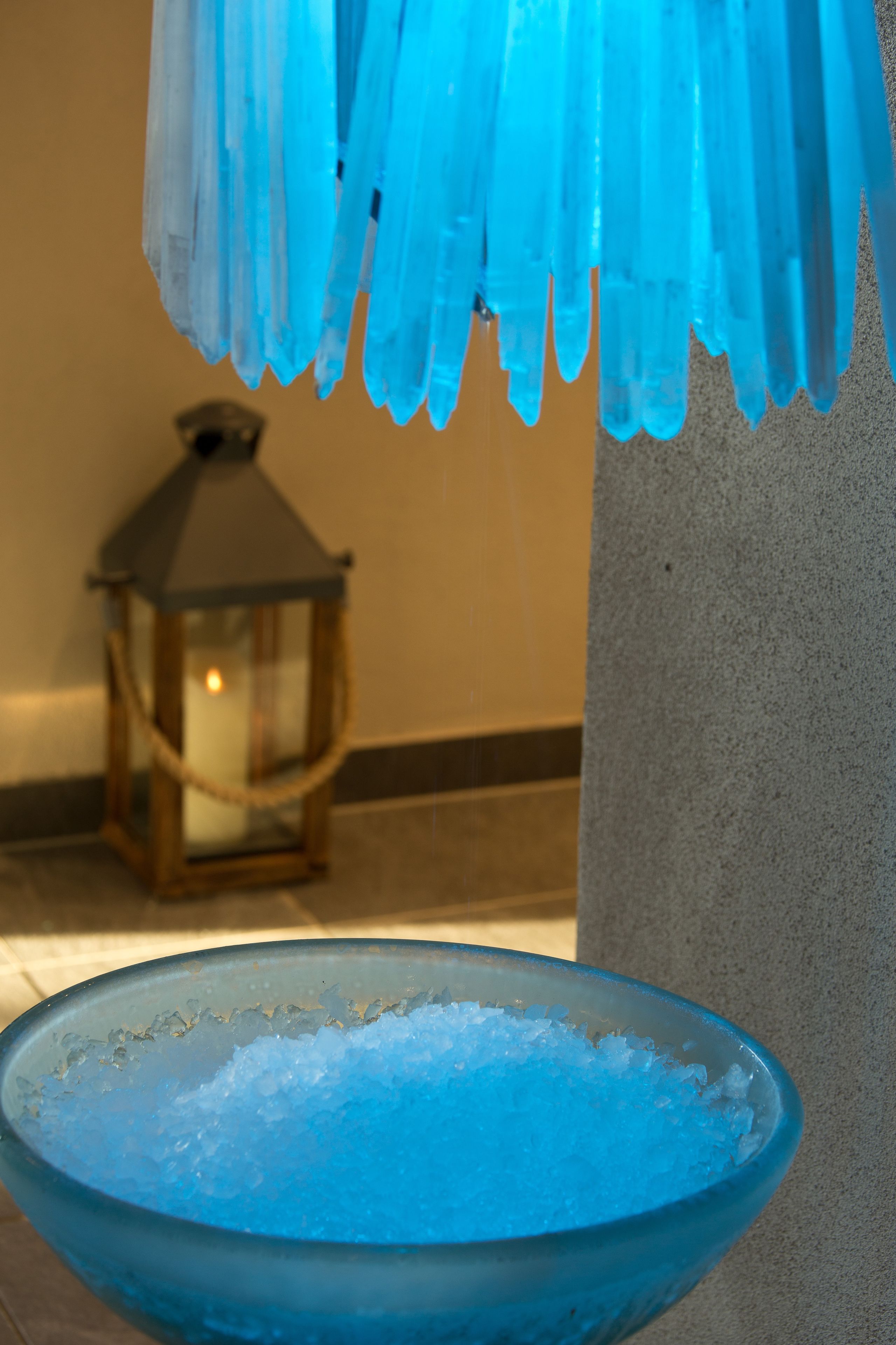 Un tazón de vidrio azul lleno de hielo, un cristal azul colgante y un farolí en el fondo.