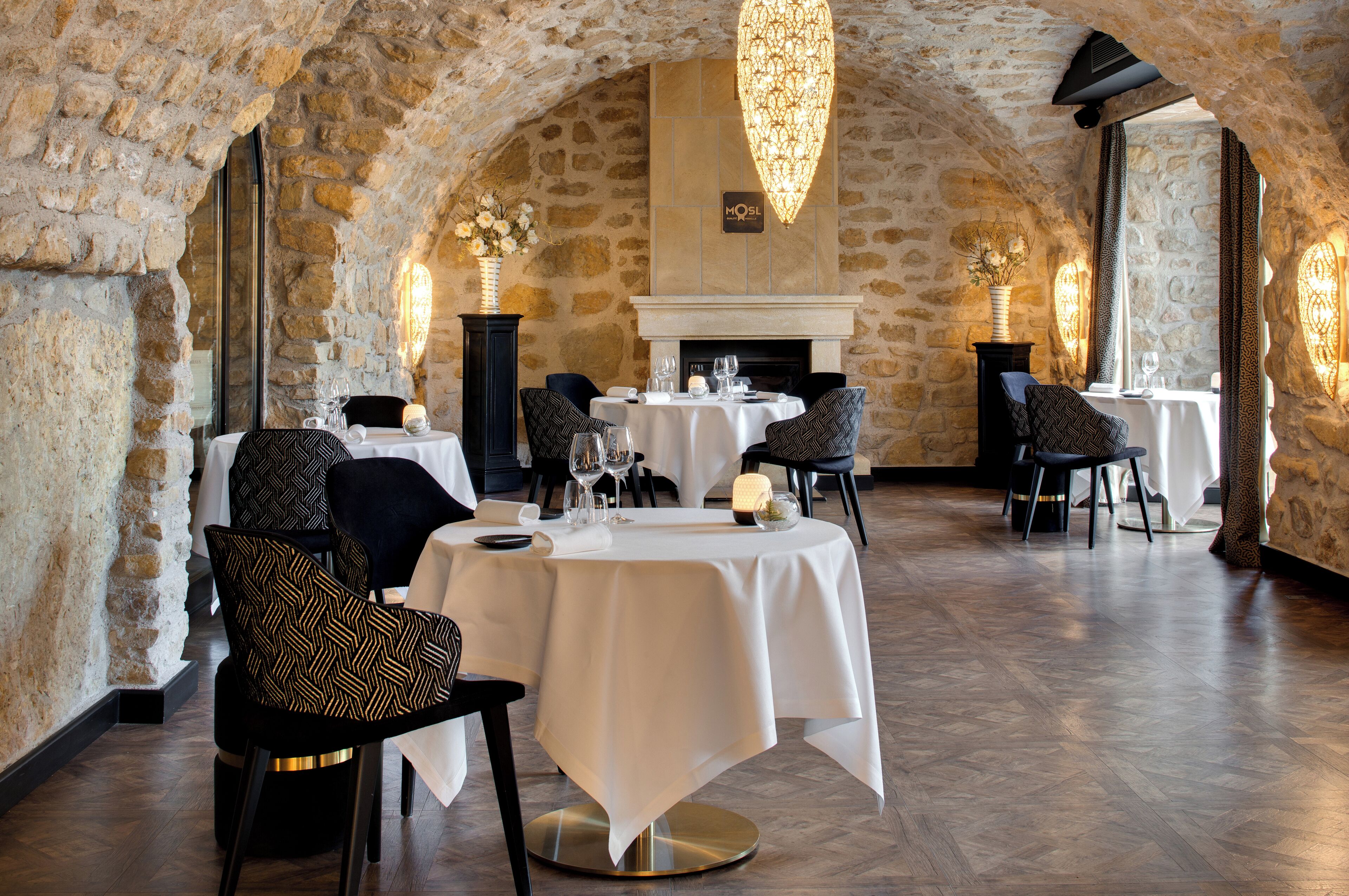 Restaurante com paredes de pedra, mesas redondas e cadeiras modernas.