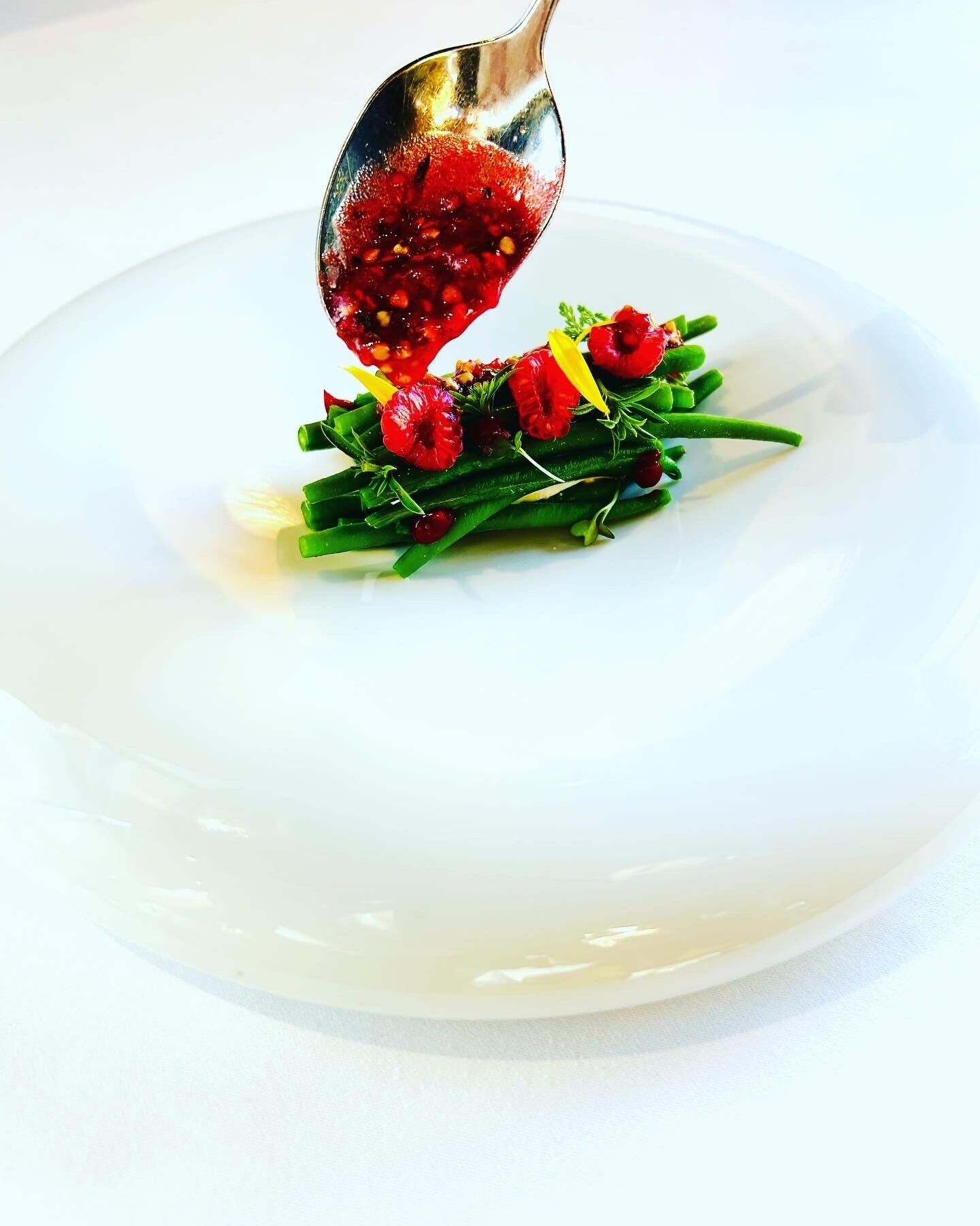 A white plate with a spoonful of red sauce and green vegetables.