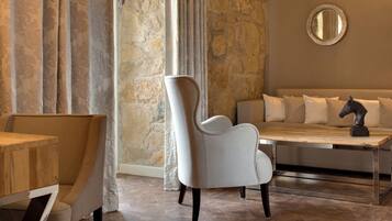 A modern room with a stone wall, a round mirror, a sofa with cushions, a white armchair, and a wooden table.