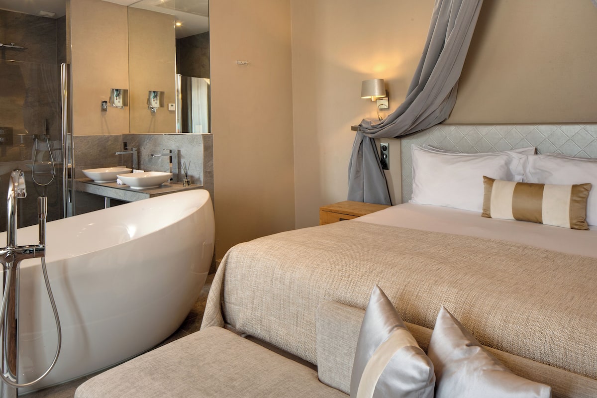 Een moderne hotelkamer met een groot bed, een aparte badkamer met bad en een grote spiegel.