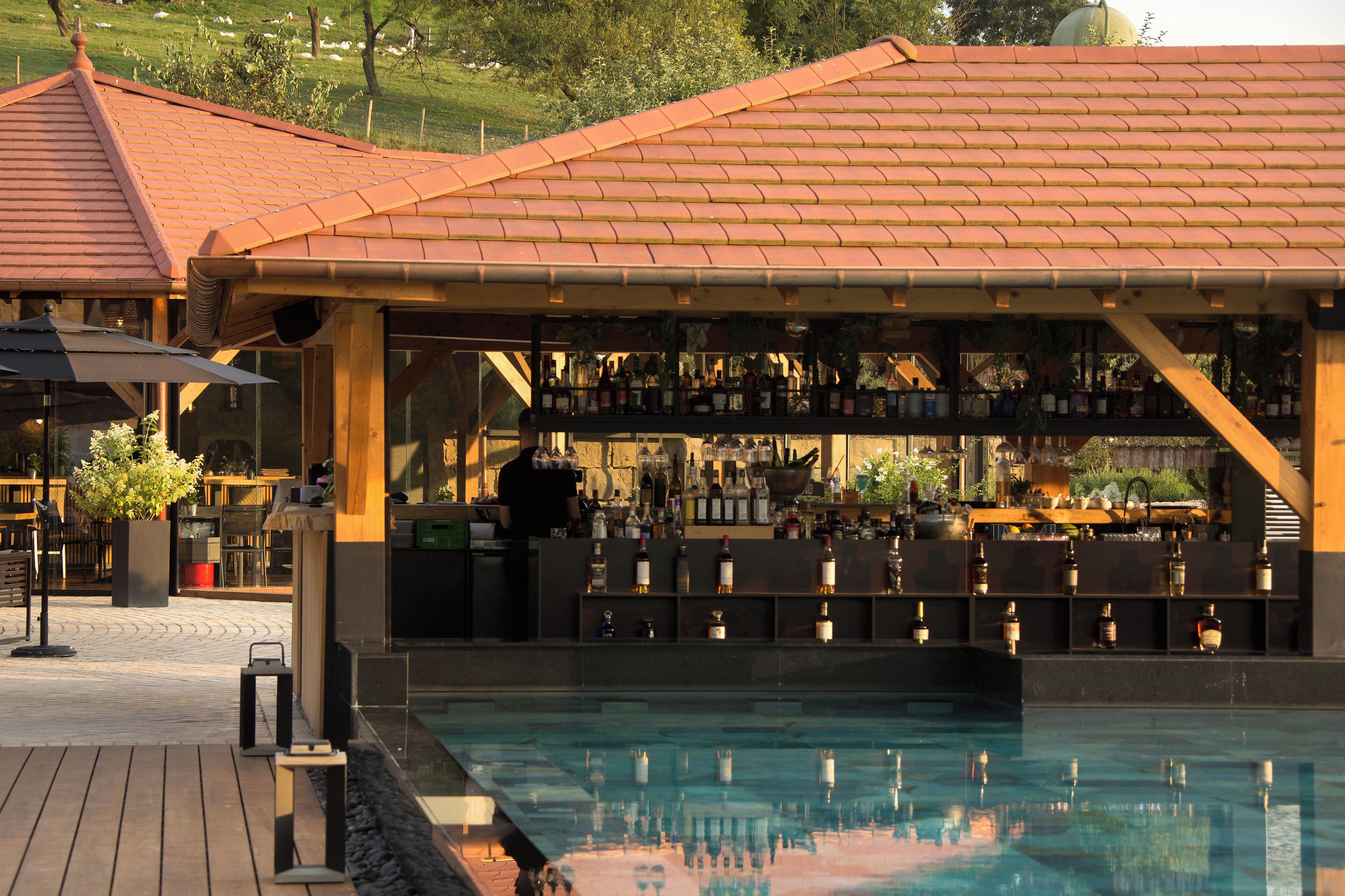 Ein Barbereich mit Pool, Holzterrasse und einem Ziegeldach.