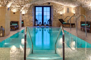 Une piscine intérieure avec des murs en pierre et une grande fenêtre.