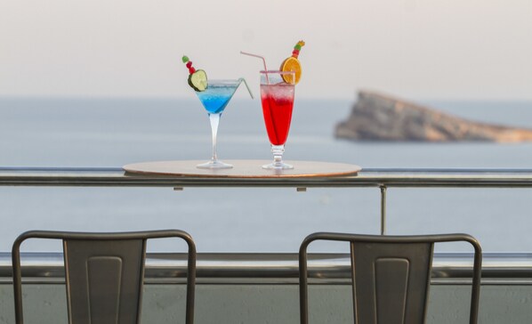 Two cocktails on a table with a view of the ocean.