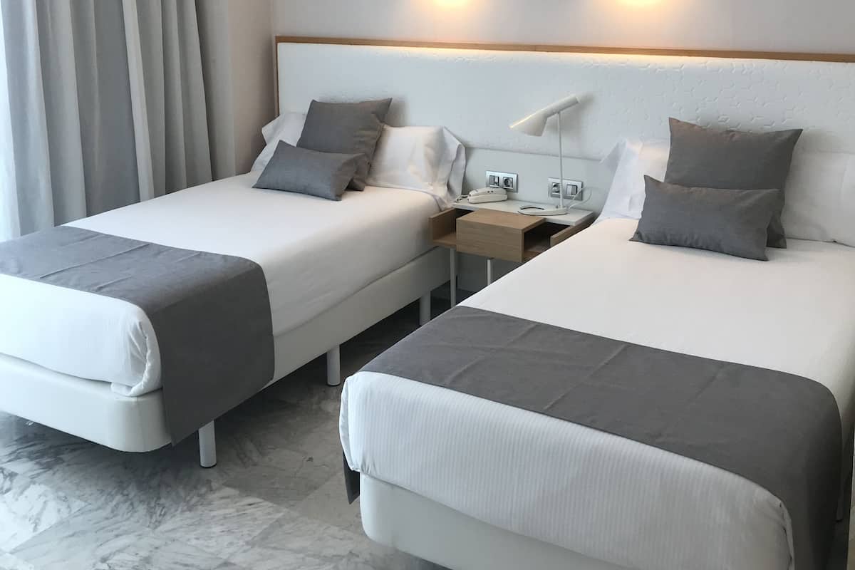 Camera d'albergo con due letti, un murale raffigurante un panorama urbano, un comodino e una lampada.