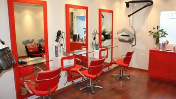 Een kapsalon met rode stoelen, spiegels en haardroger.
