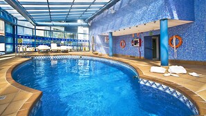 An indoor swimming pool with clear blue water, a tiled wall, and a glass ceiling. - Madeira Centro (Benidorm)