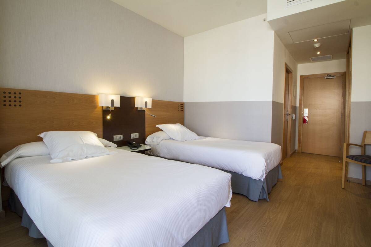 Una camera d'albergo con due letti, una testiera in legno, un comodino e una lampada a parete.