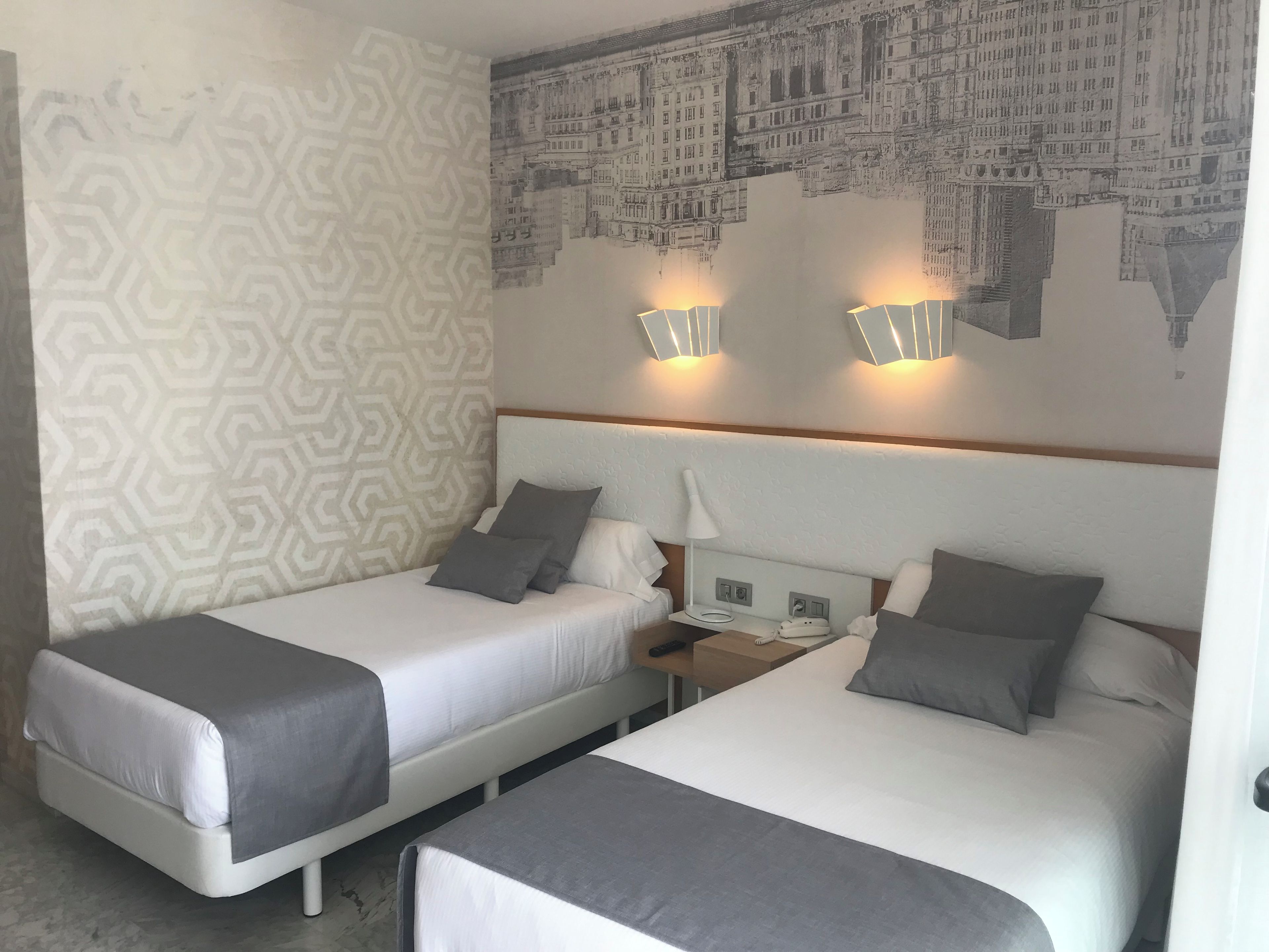 Una habitació d'hotel amb dos llits individuals, una paret amb dibuixos i un mural de paisatge urbà.