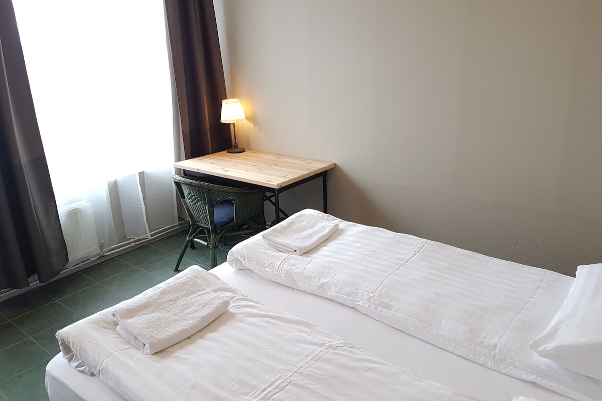 Ett hotellrum med två sängar, ett skrivbord, en stol och en lampa.