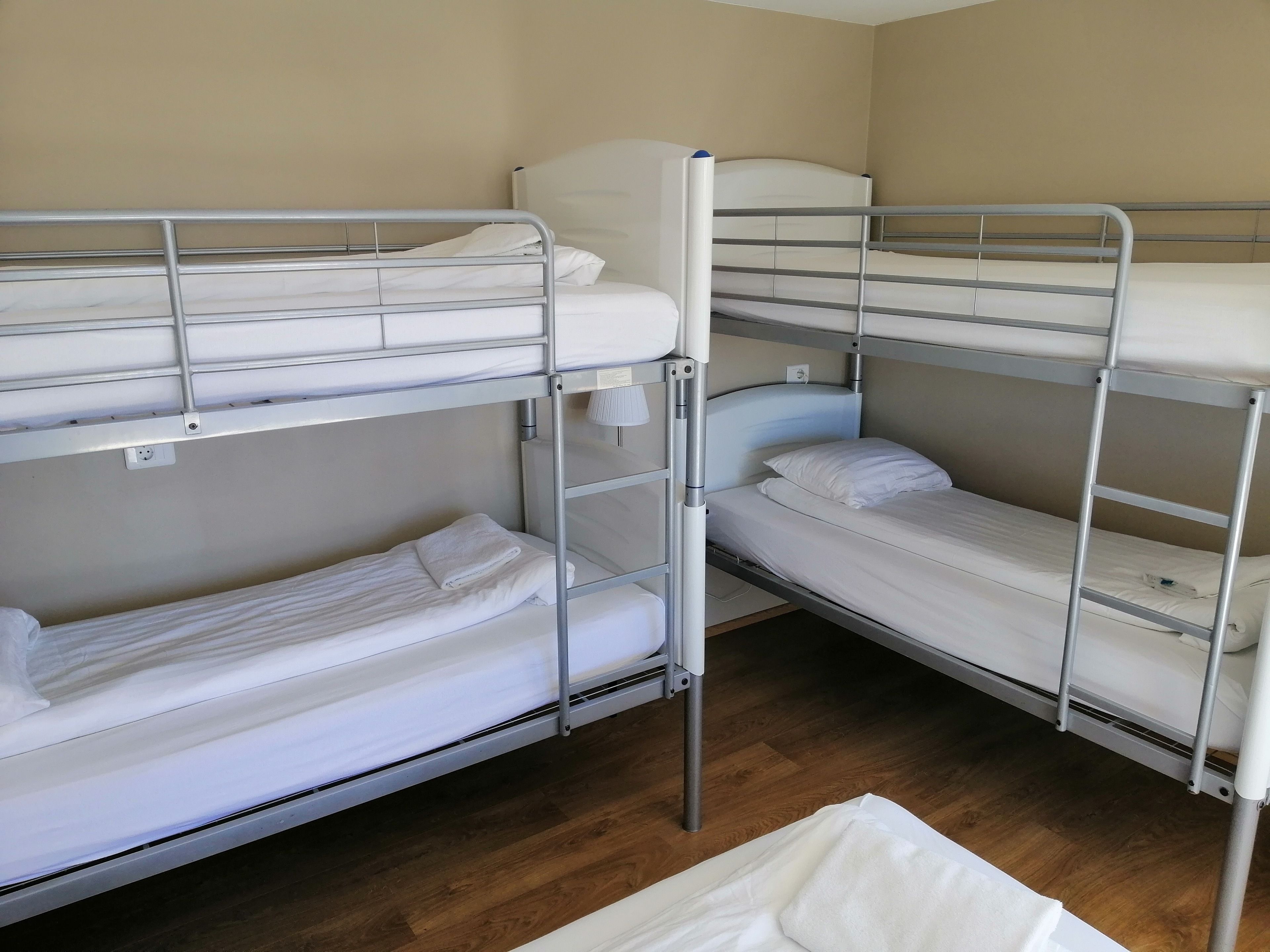 Habitación con literas, suelo de madera, ropa de cama blanca y una mesita con lámpara.