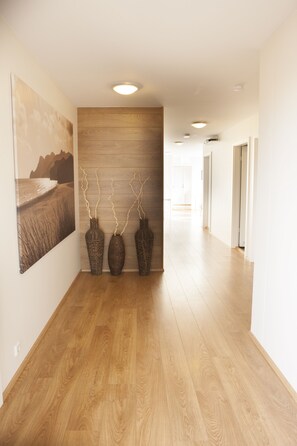 A hallway with wooden flooring, a wall-mounted painting, and three wicker vases with branches. - Lyngás Guesthouse (Egilsstaðir)