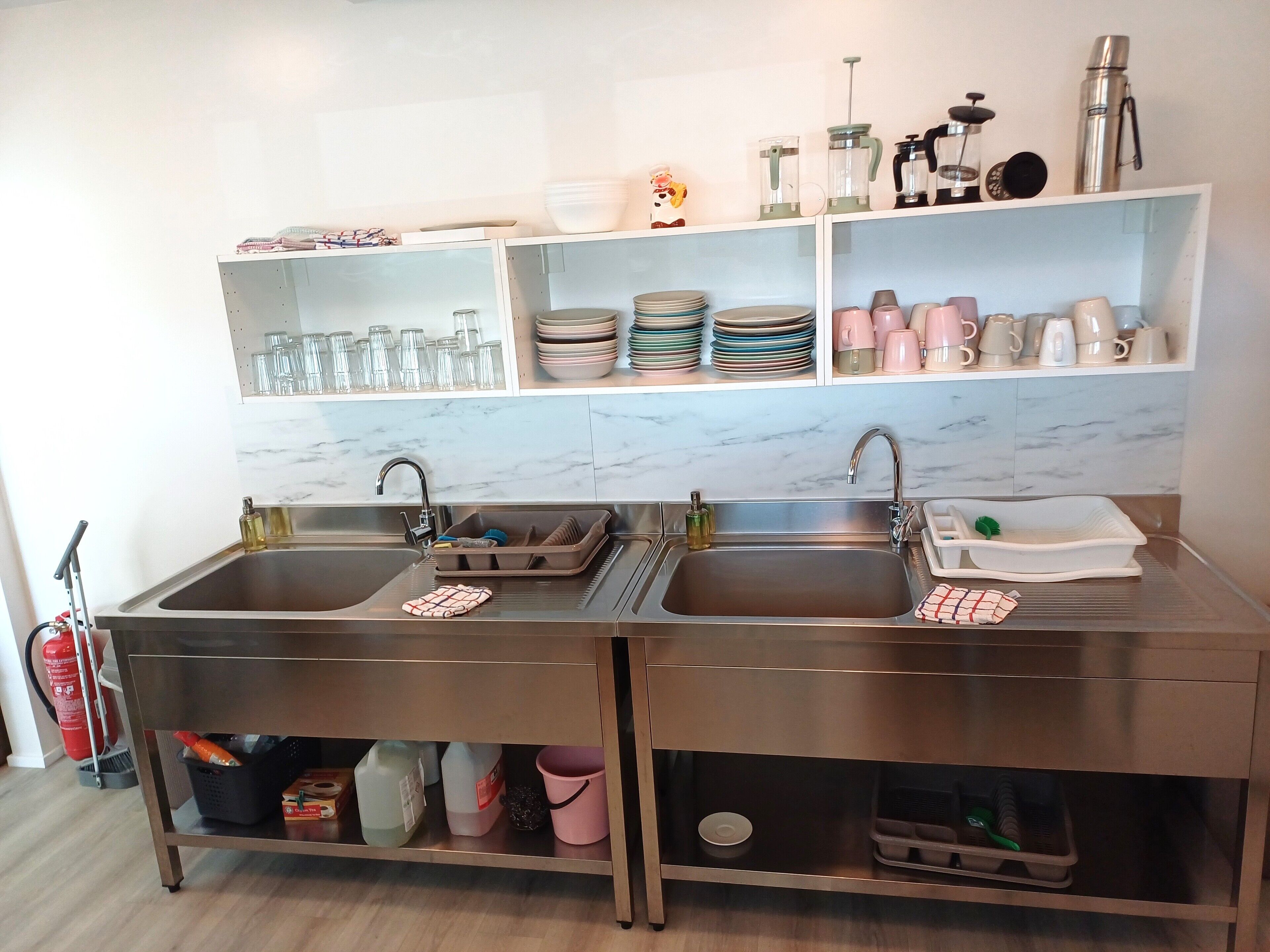 A modern kitchen with two sinks, a marble backsplash, and shelves with glassware and plates.