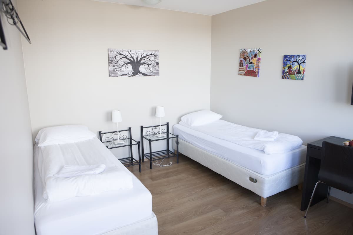 Ett hotellrum med två separata sängar, ett litet bord med stolar och två tavlor som hänger på väggen.
