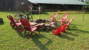 Una cabaña rústica con un hogar de piedra rodeado de sillas Adirondack rojas.