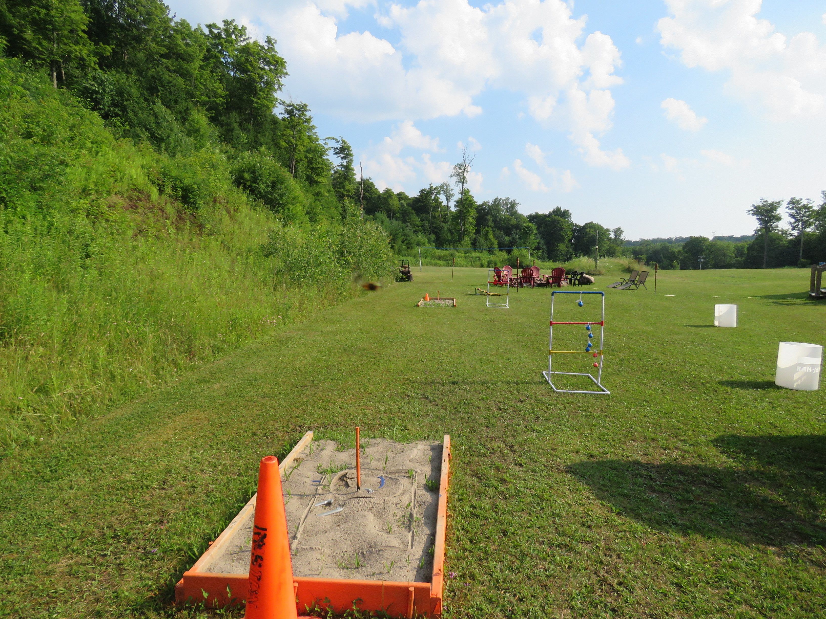 A grassy field with a sandbox, outdoor furniture, and a swing set.