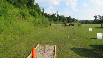 A grassy field with a sandbox, outdoor furniture, and a swing set.
