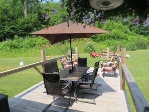 An outdoor patio with a table and chairs, surrounded by a wooden deck and a view of a lush garden. - Tug Hill Resort (Redfield)