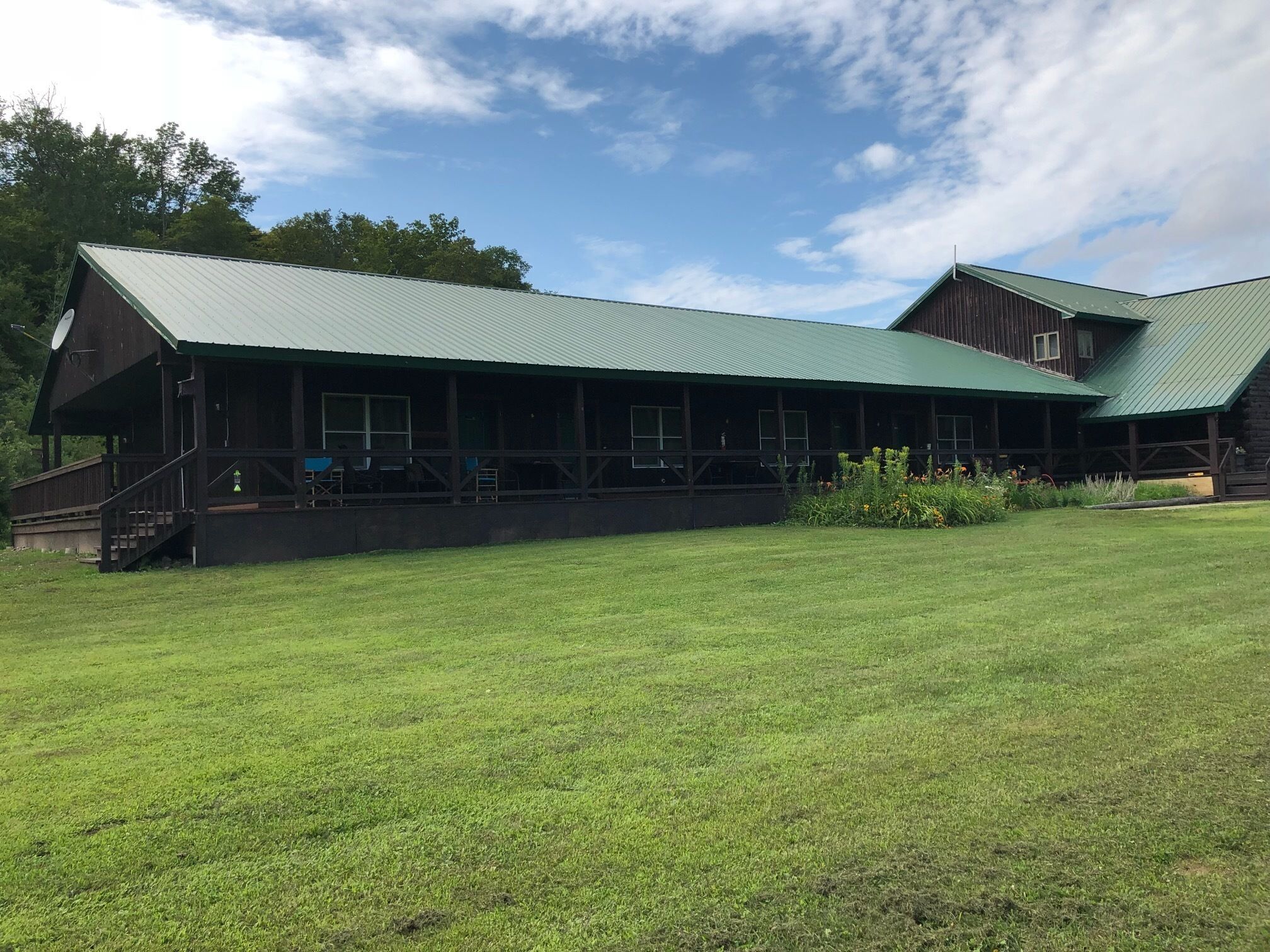 A rustic lodge with a green metal roof, a covered porch, and a grassy lawn.