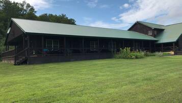 A rustic lodge with a green metal roof, a covered porch, and a grassy lawn.