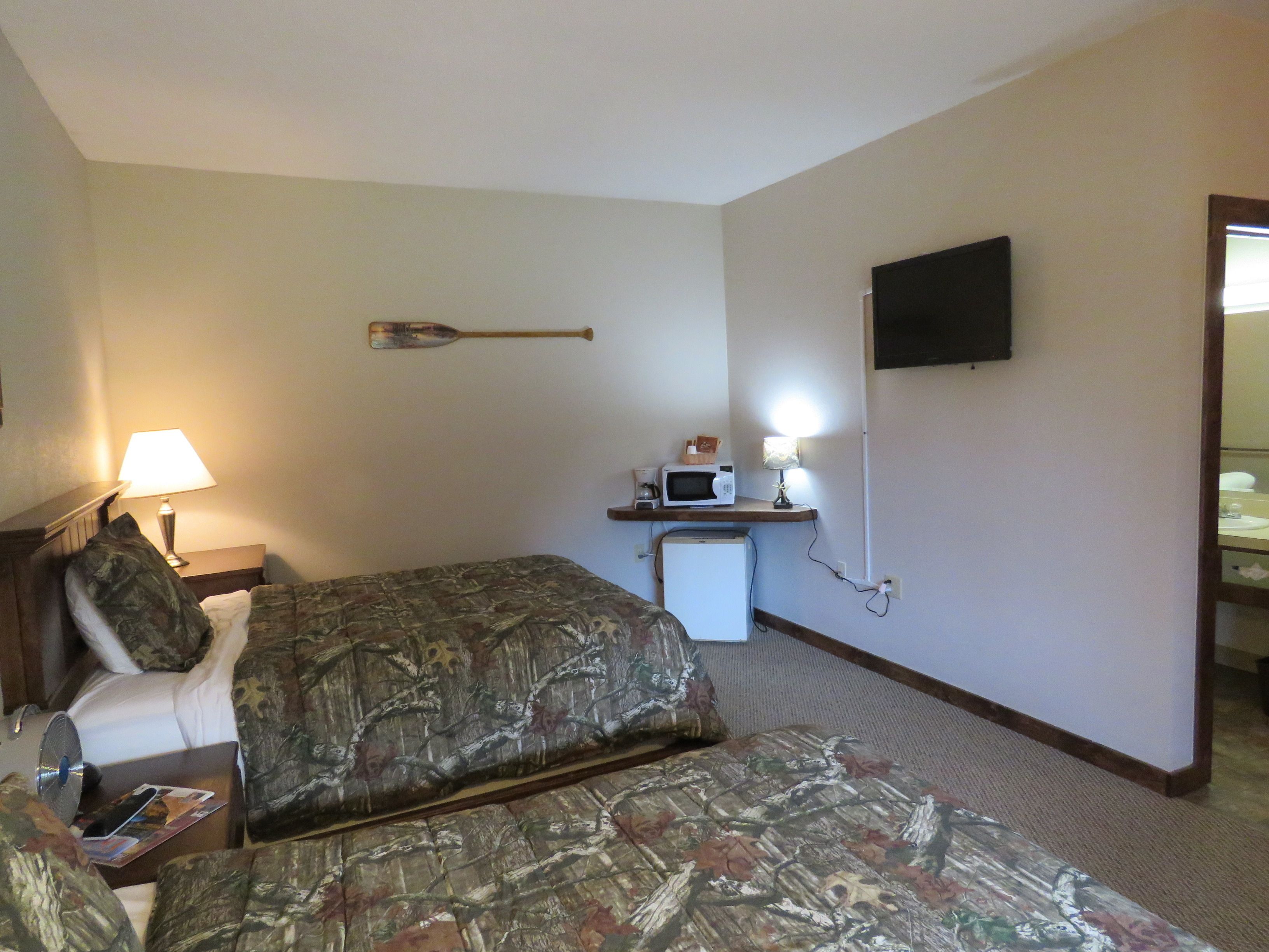 Een hotelkamer met twee bedden, een bureau met een magnetron, een televisie en een kleine koelkast.