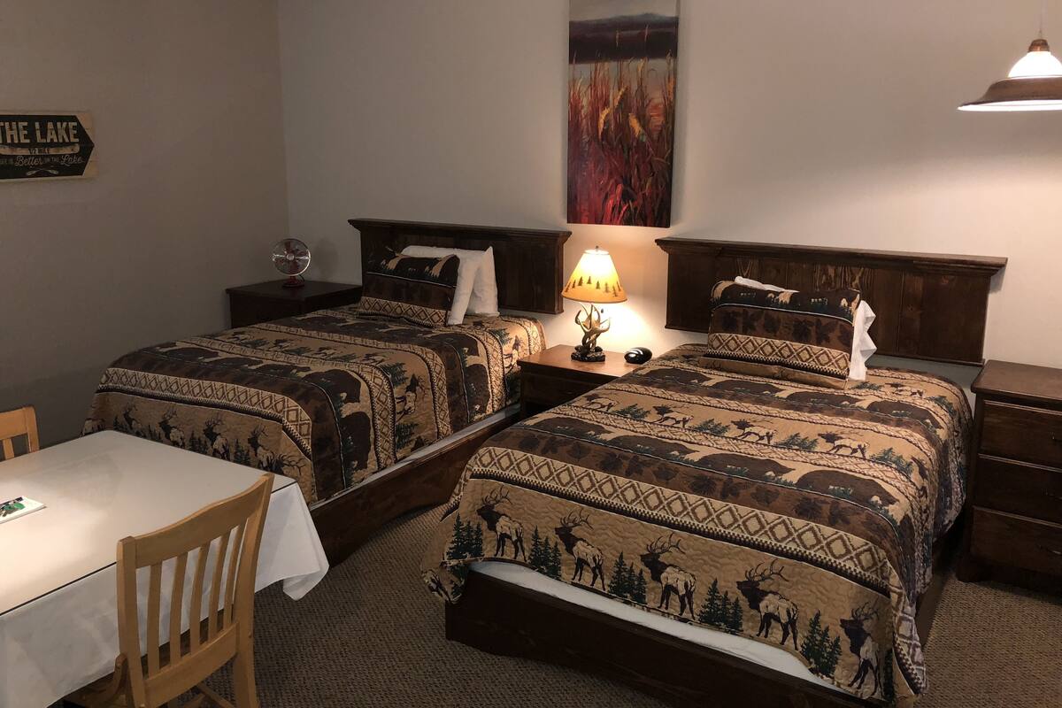 A hotel room with two beds, a table, and a chair.