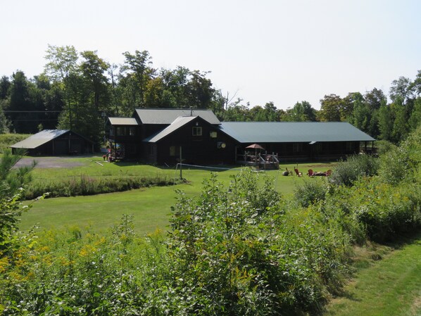A large log cabin with a green roof, surrounded by a well-maintained lawn and dense greenery. - Tug Hill Resort (Redfield)