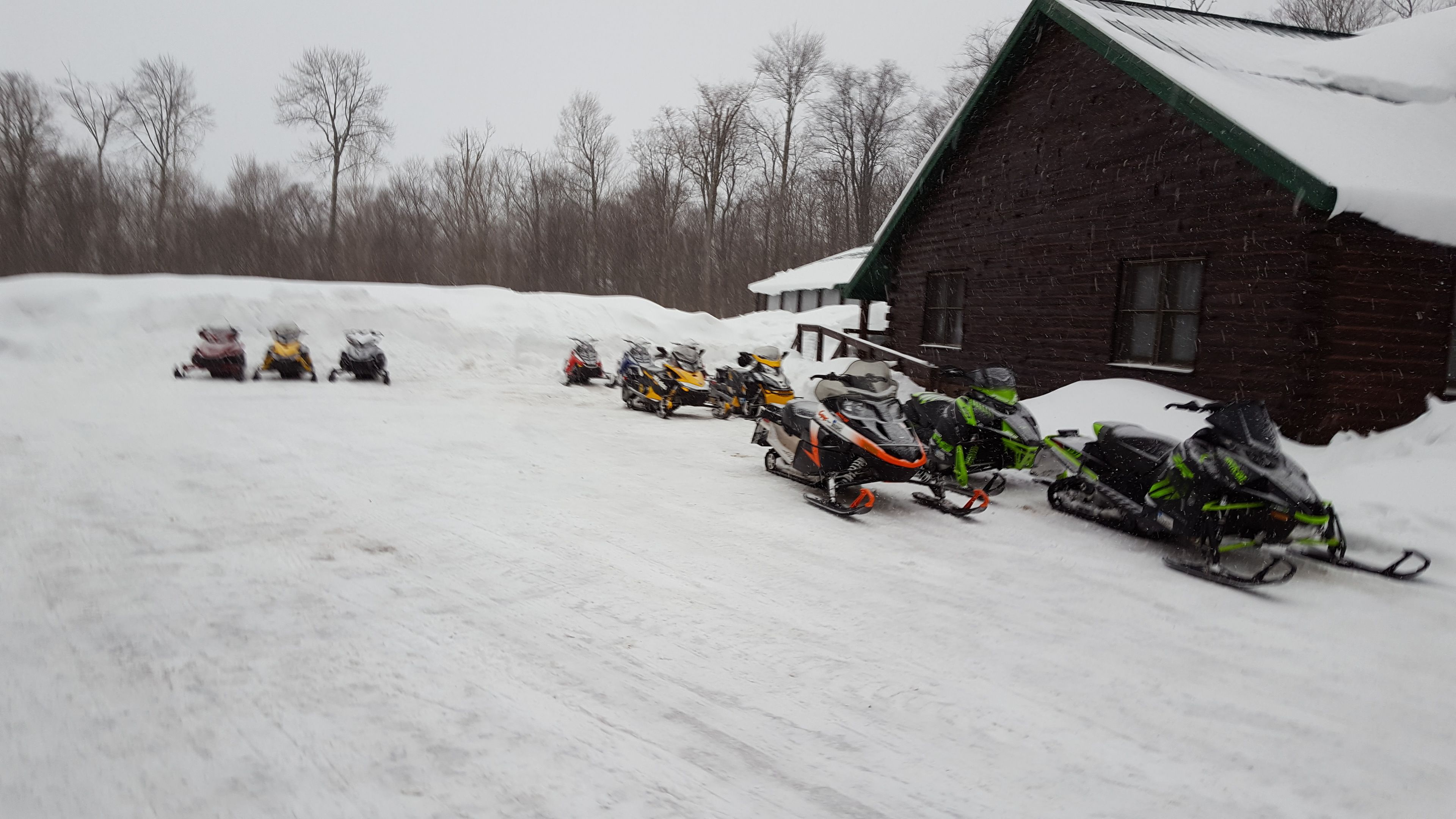 A snow-covered landscape with several snowmobiles parked in front of a wooden building.
