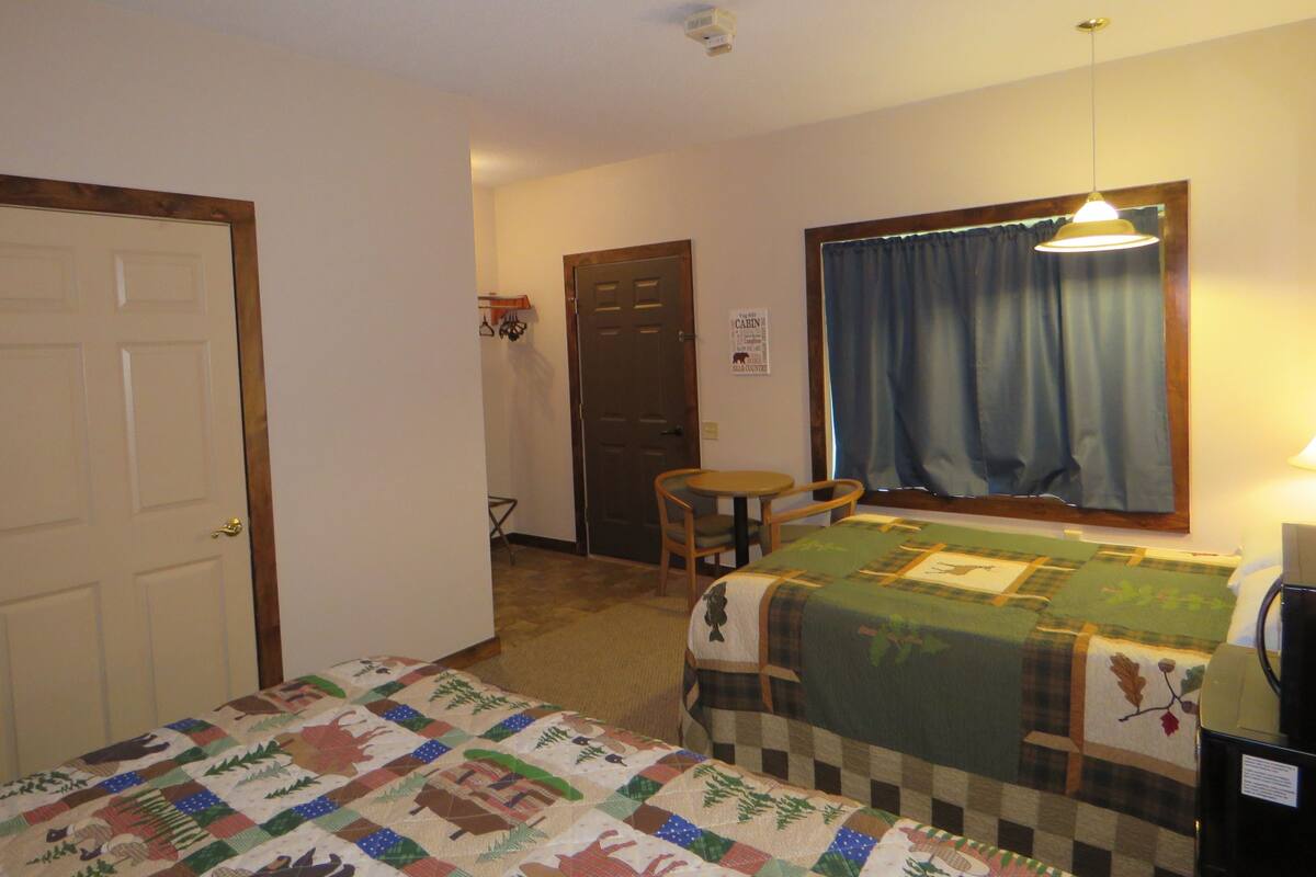 A room with two beds, a desk, a chair, a window with curtains, and a door.
