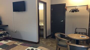 Habitación de hotel con cama, televisión, escritorio y silla, y una puerta que da a un baño.