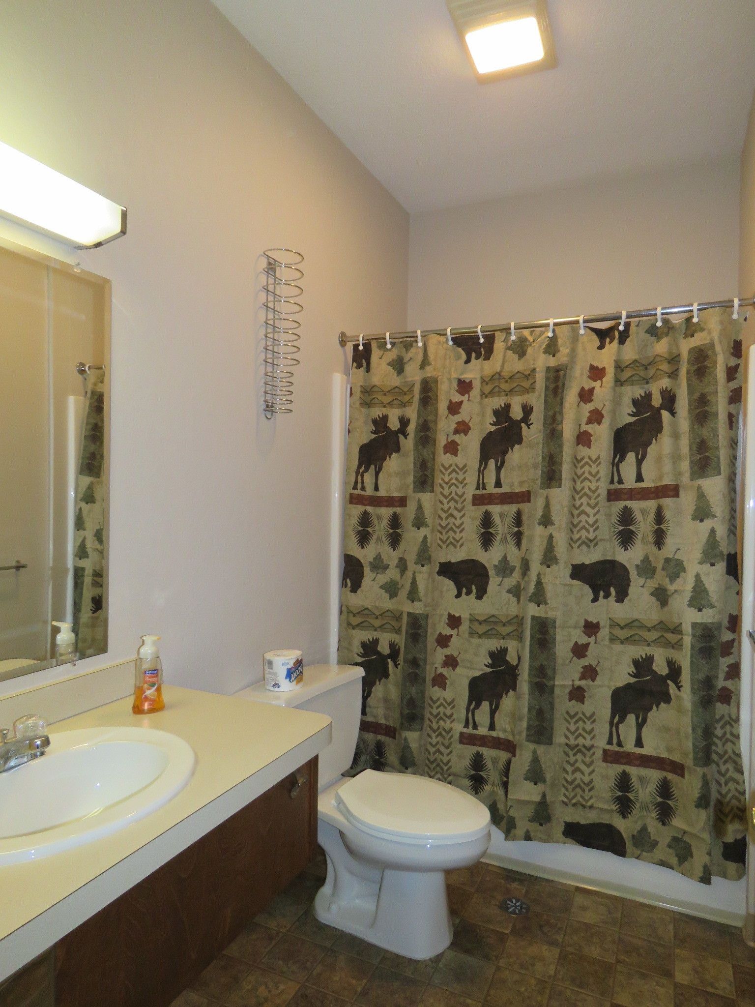 A bathroom with a toilet, sink, and shower curtain featuring a moose and leaf pattern.