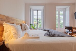 Habitación de hotel con cama, una silla, una mesa y balcón con vistas.