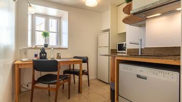Une cuisine compacte comprenant une table à manger, des chaises, un réfrigérateur, un lave-vaisselle et une fenêtre agrémentée d’une plante.