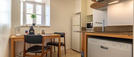 Una cocina compacta con una mesa de comedor, sillas, un refrigerador, un lavavajillas y una ventana con una planta.