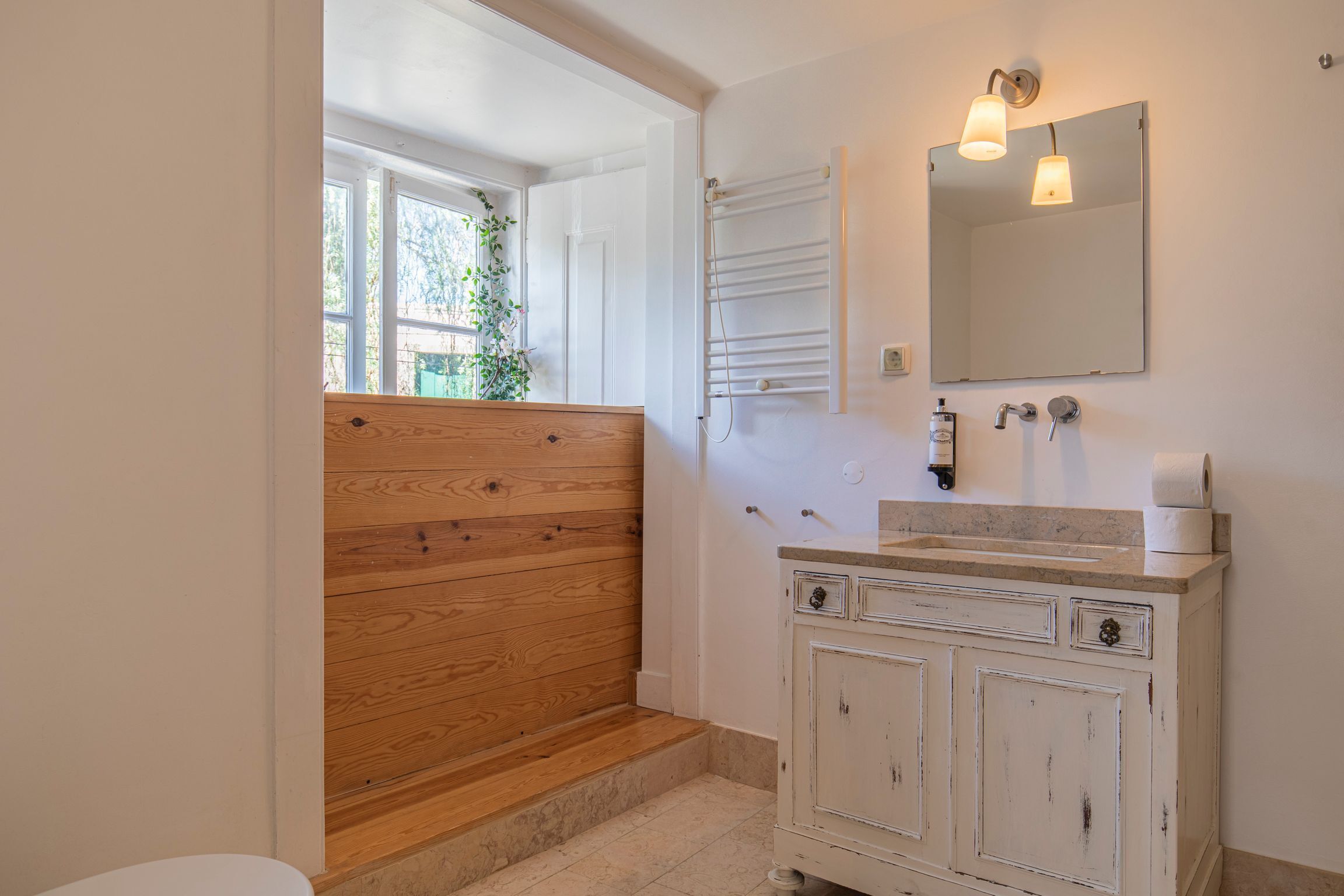 Une salle de bain avec un banc en bois, un meuble-lavabo blanc avec un miroir et un porte-serviettes.