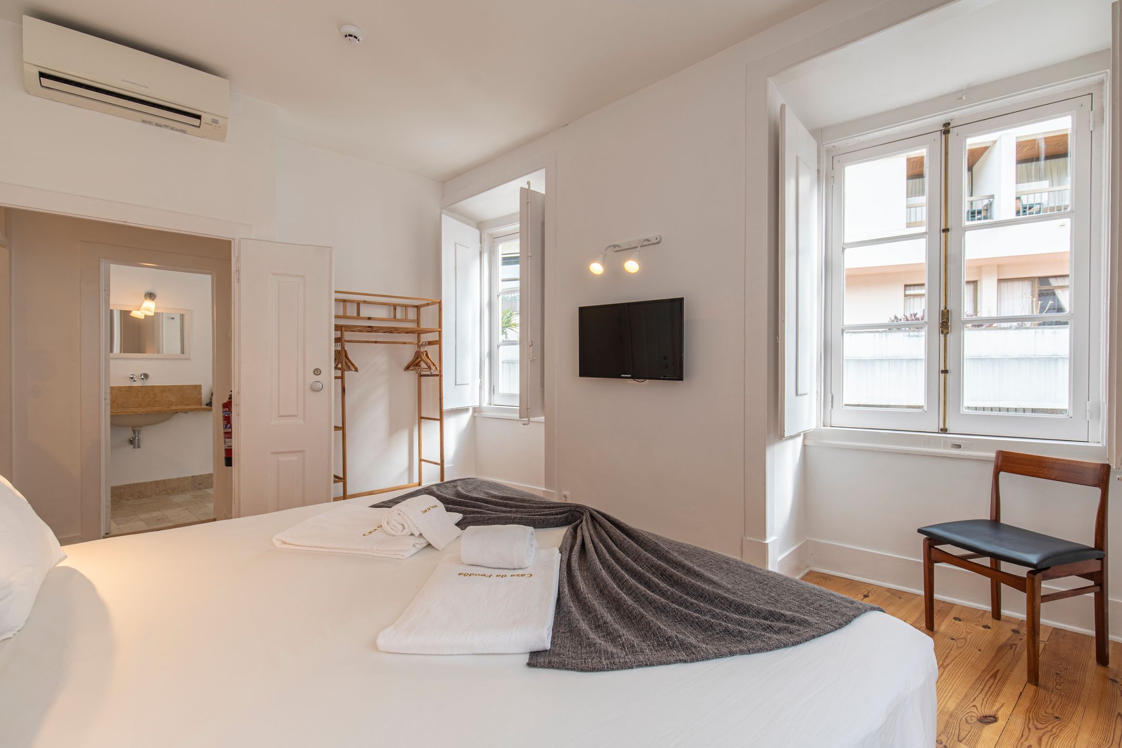 A hotel room with a bed, a TV, a chair, and a window with a view of buildings.