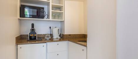 Cocina compacta con armarios blancos, microondas, cafetera y lavabo.