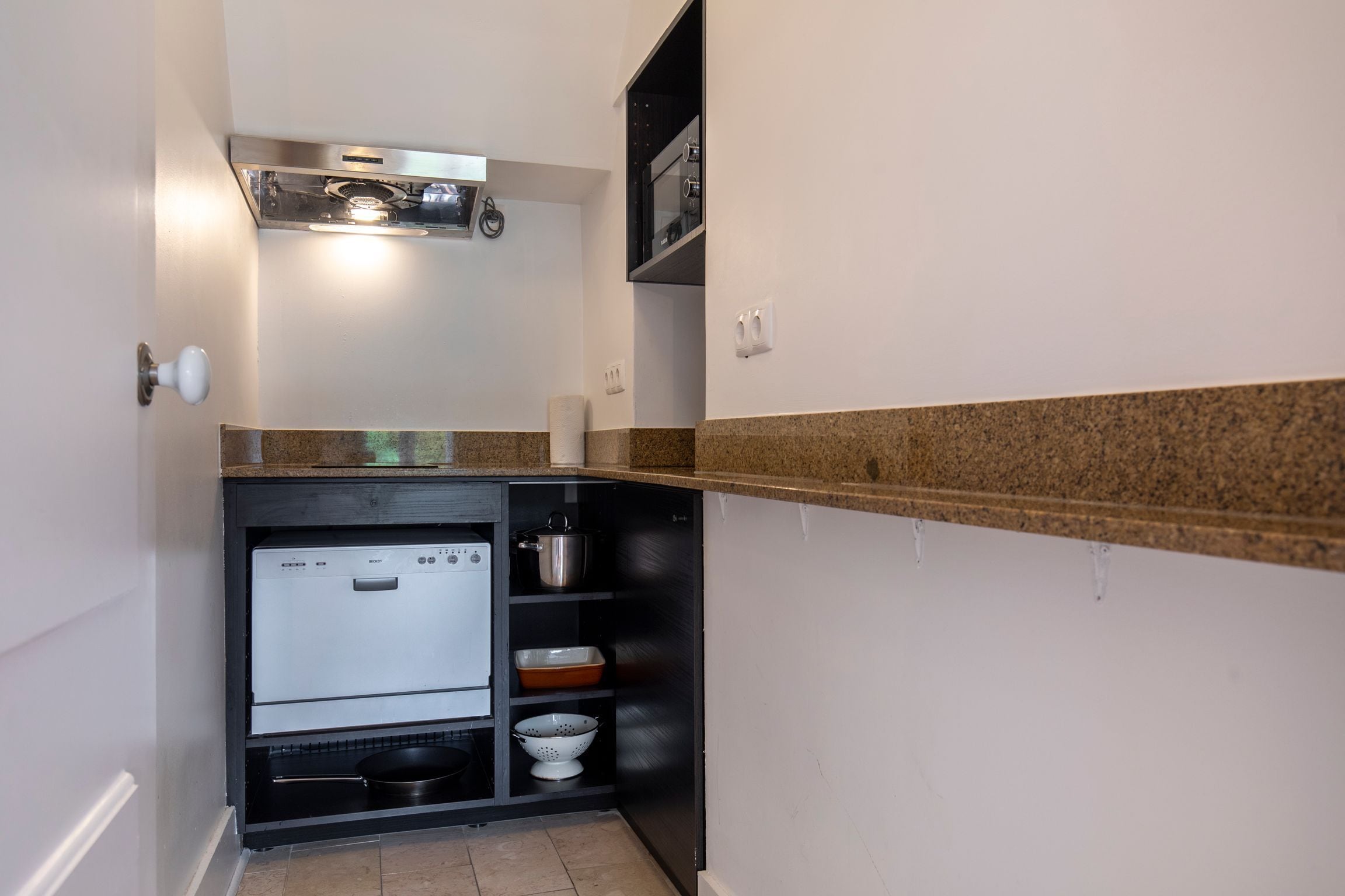 A compact kitchen with a built-in refrigerator, a microwave, and a stove. There are shelves with kitchenware and a countertop with a sink.
