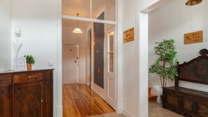 A hallway with wooden flooring, a dark wooden bench, a potted plant, and a sign indicating apartment numbers. - Pendoa sintra collection (Sintra)
