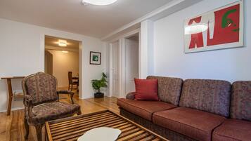 A living room with a wooden coffee table, a patterned sofa, a vintage armchair, and a framed picture on the wall.