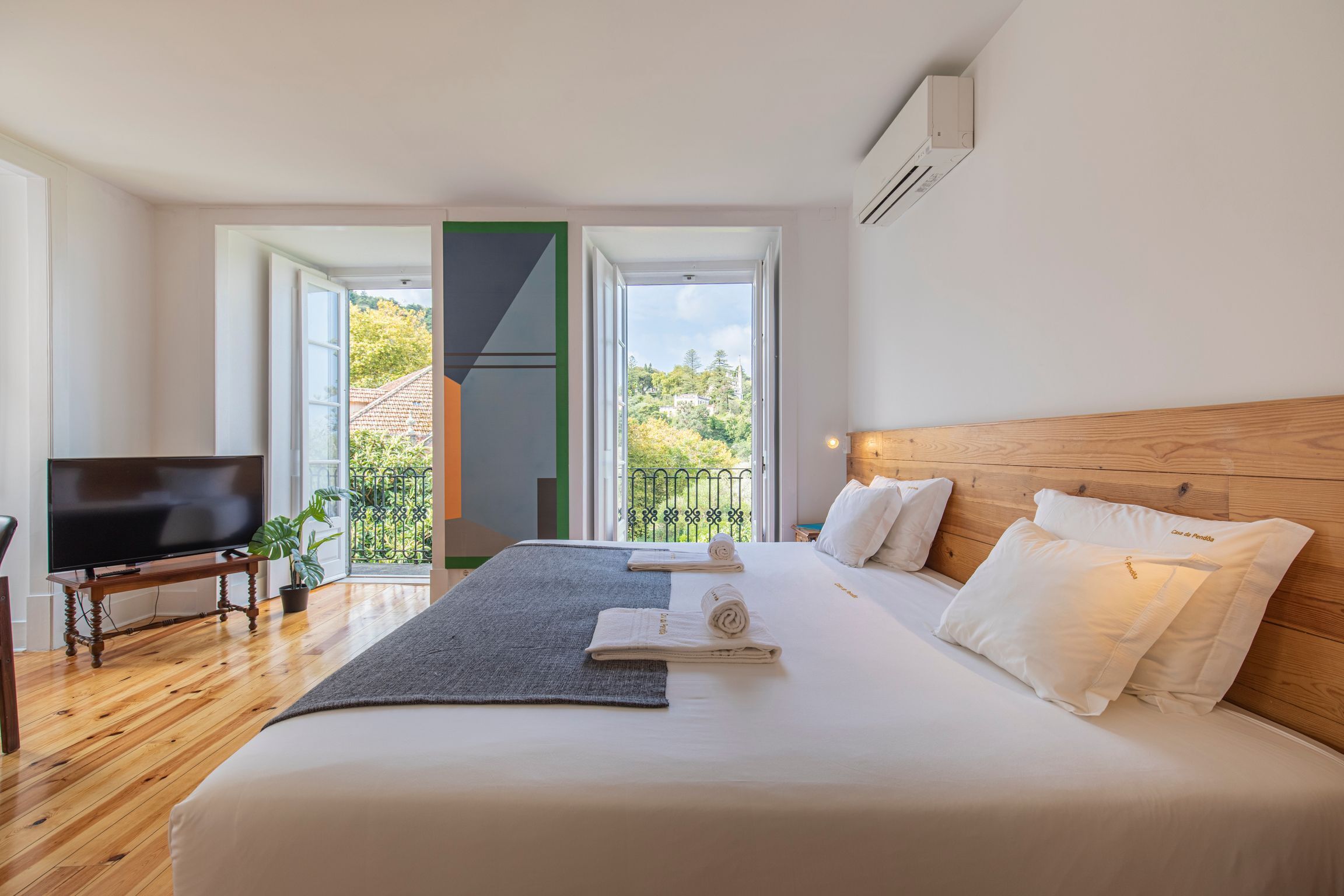 Une chambre d’hôtel moderne dotée d’un grand lit, d’une télévision à écran plat et d’un balcon offrant une vue sur la verdure.