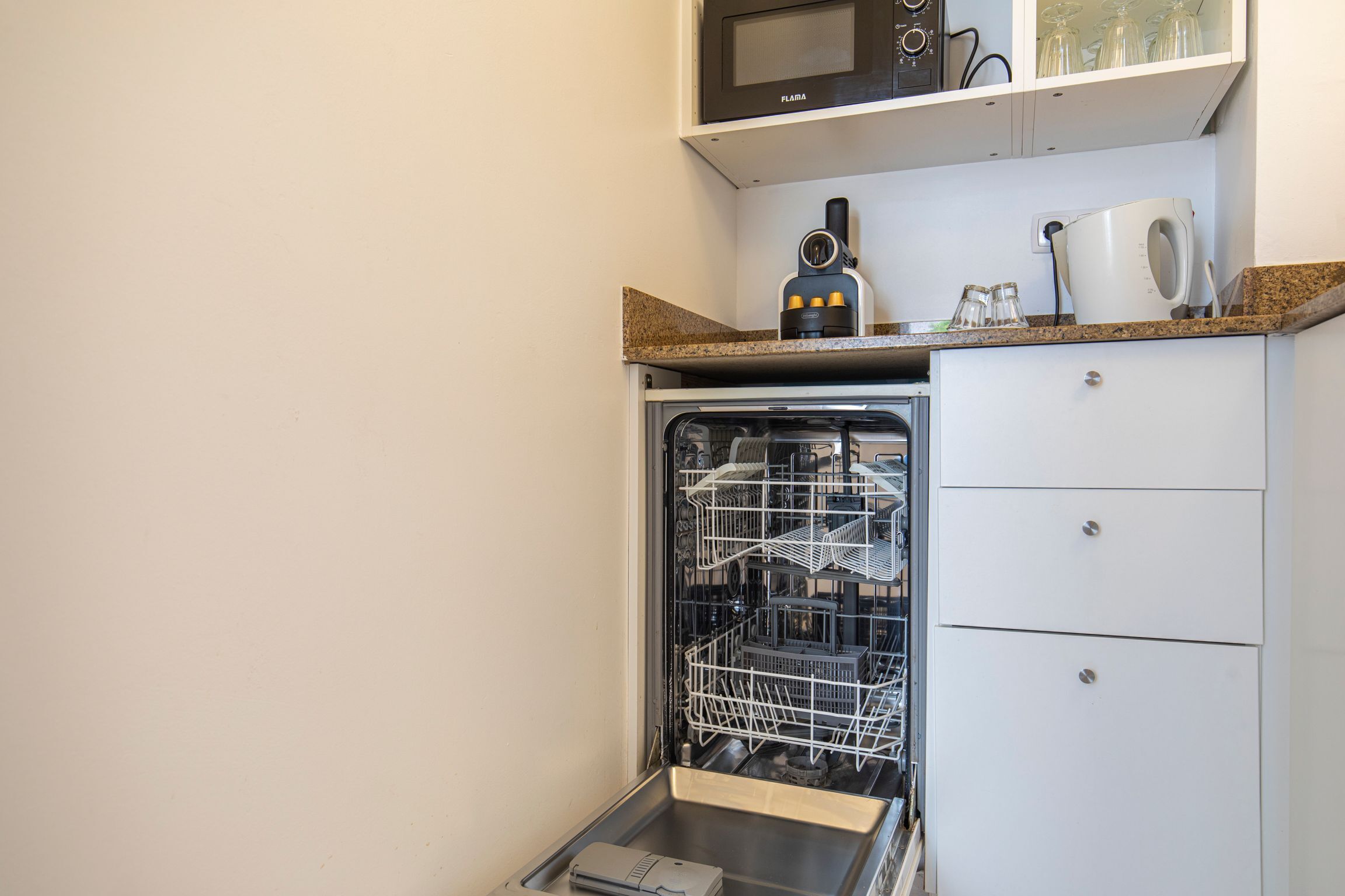 Een kleine keuken met een magnetron, koffiezetapparaat en vaatwasser.