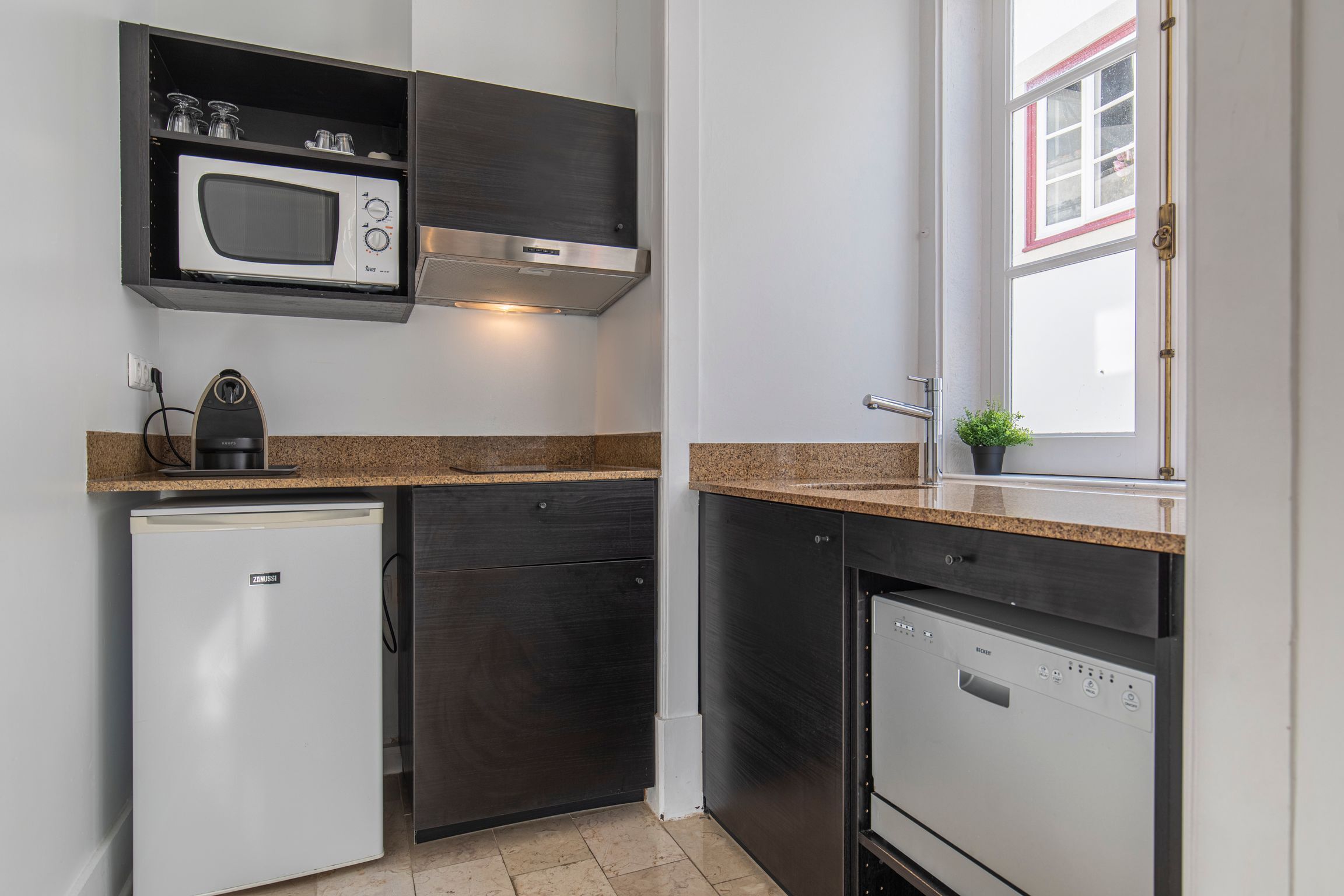 A compact kitchen with a built-in microwave, a small refrigerator, and a dishwasher.