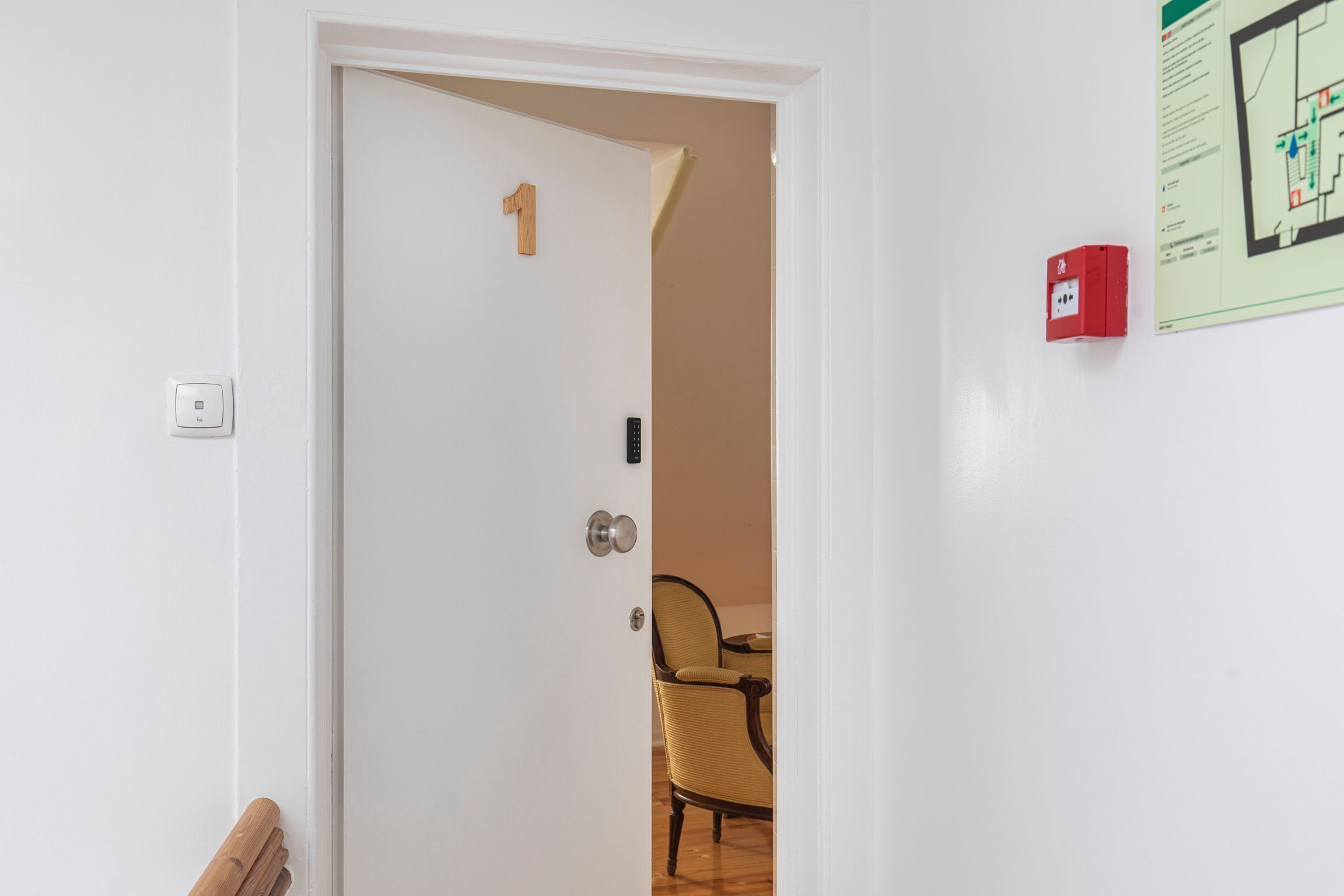 A room with a white door marked with the number 1, a red fire alarm, and a wall-mounted map.