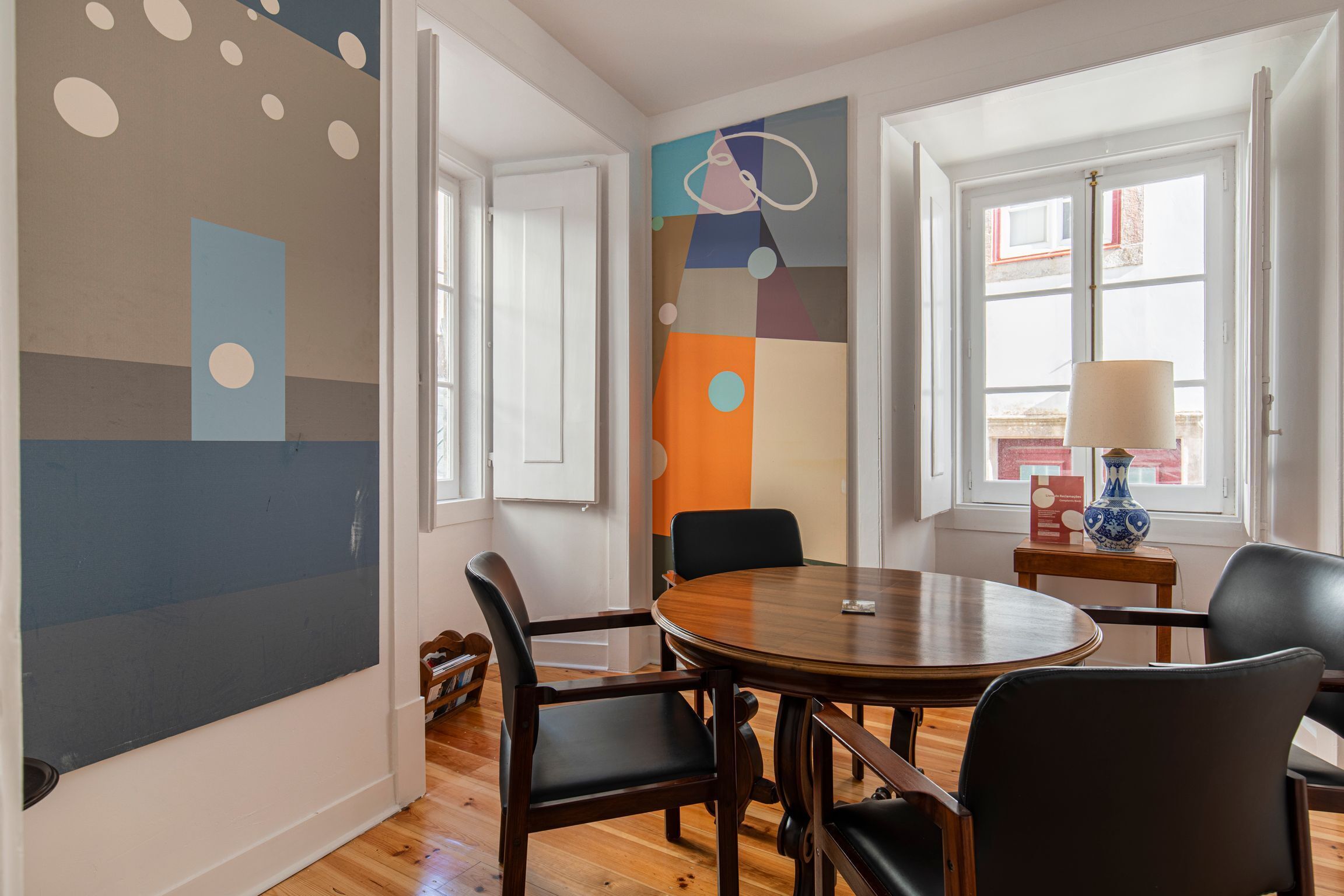 A dining area with a round wooden table, black chairs, and a colorful abstract painting on the wall.