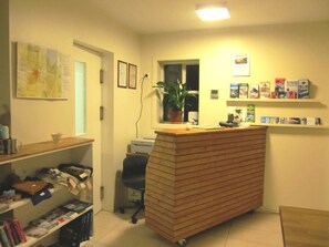 A reception desk with a computer, a potted plant, and a window. There are shelves with books and a map on the wall.